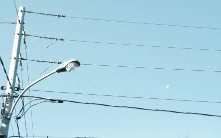 HD PC desktop wallpaper showing man-made power lines and a streetlight crossing a pale blue sky with a small crescent moon.
