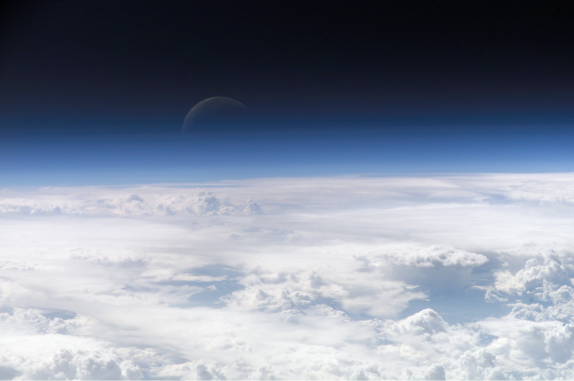 A stunning HD desktop wallpaper featuring a sci-fi sky, with fluffy clouds beneath a vast expanse of space and a faint celestial body in the distance.