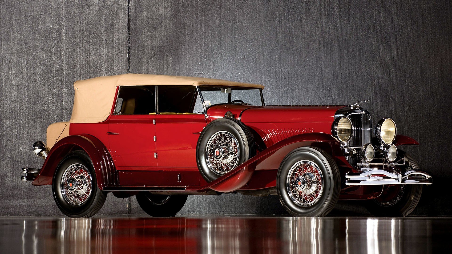 HD PC desktop wallpaper featuring a classic red Duesenberg Model J vintage vehicle with beige soft top, set against a textured gray background.