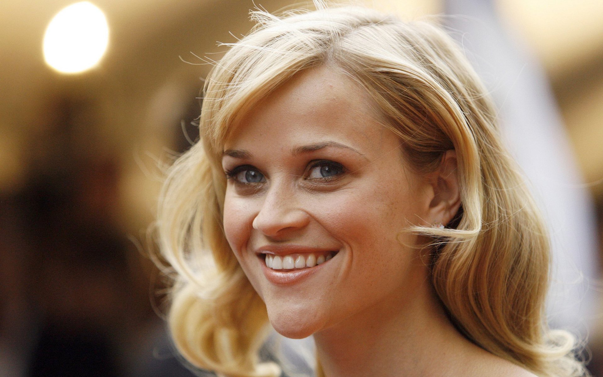 HD PC desktop wallpaper featuring a close-up portrait of celebrity Reese Witherspoon smiling with soft lighting in the background.