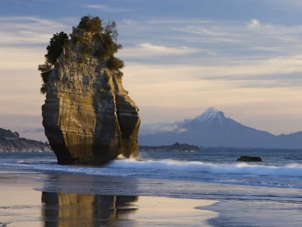 HD desktop wallpaper featuring a striking rock formation along a tranquil shoreline, with a distant snow-capped mountain under a partly cloudy sky. Nature, rock.