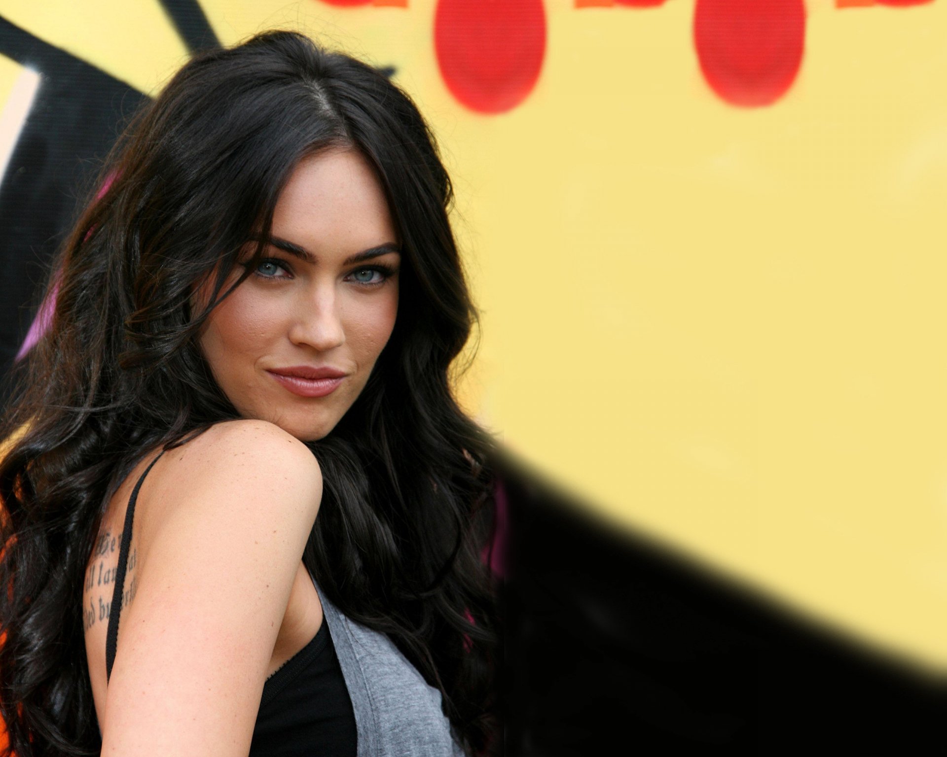 Megan Fox poses confidently in front of a vibrant yellow background, captured in stunning HD, making this an eye-catching desktop wallpaper.