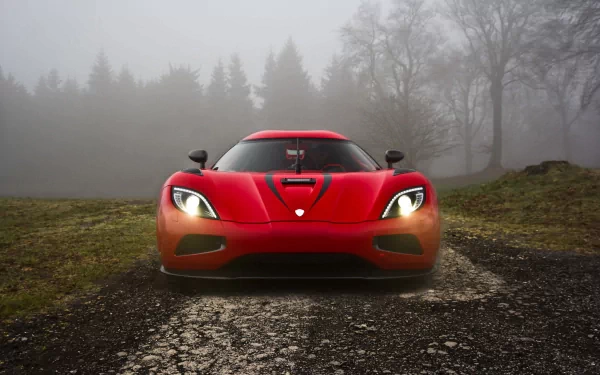HD desktop wallpaper featuring a striking front view of a red Koenigsegg Agera, illuminated headlights and foggy forest background creating an atmospheric scene.