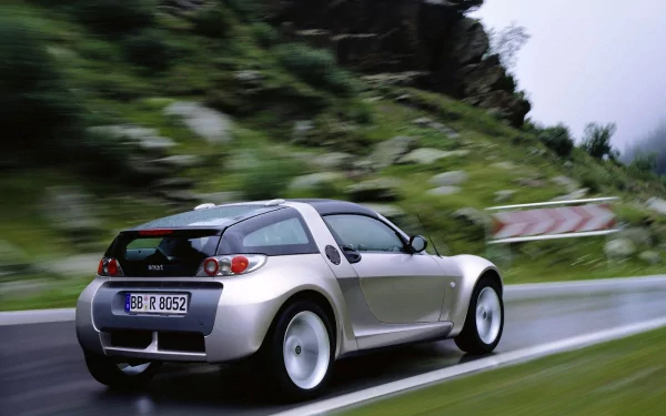 A sleek Smart vehicle speeding along a winding road, set against a backdrop of lush greenery, showcased in high-definition as a striking desktop wallpaper.