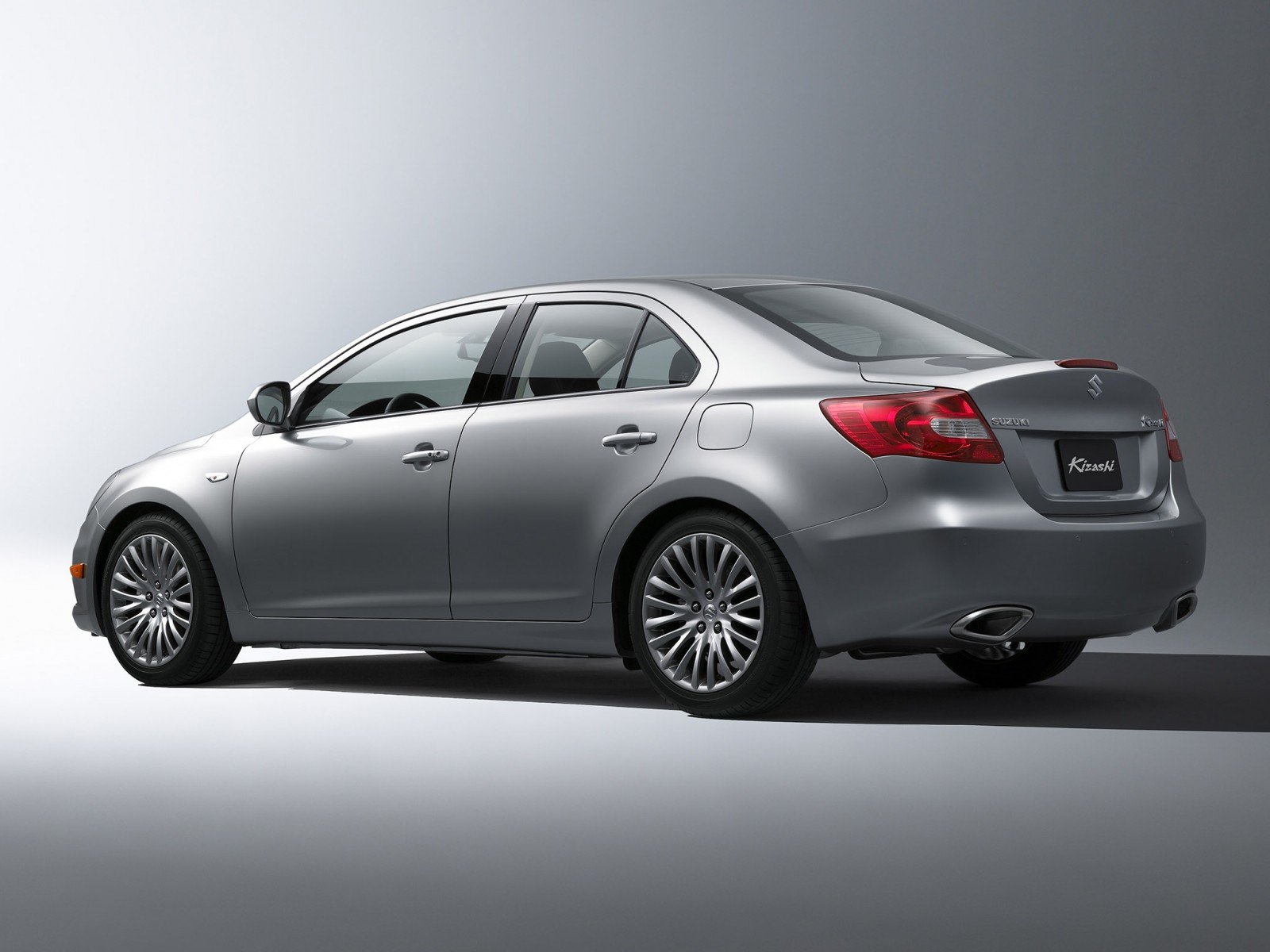 Silver Suzuki sedan shown from rear three-quarter view on a neutral gray backdrop — HD PC desktop wallpaper and background.