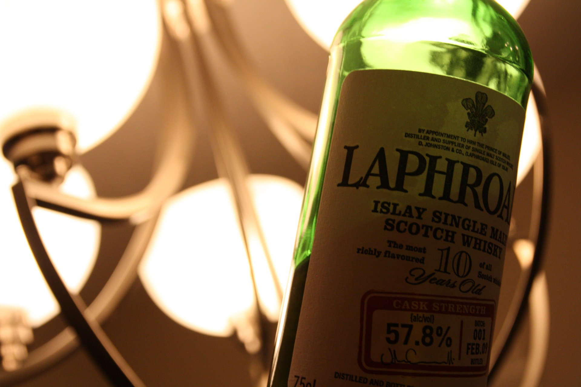 4K Ultra HD PC desktop wallpaper: close-up of a green Laphroaig whisky bottle tilted beside a warm chandelier light, shallow depth-of-field, food and whisky theme.