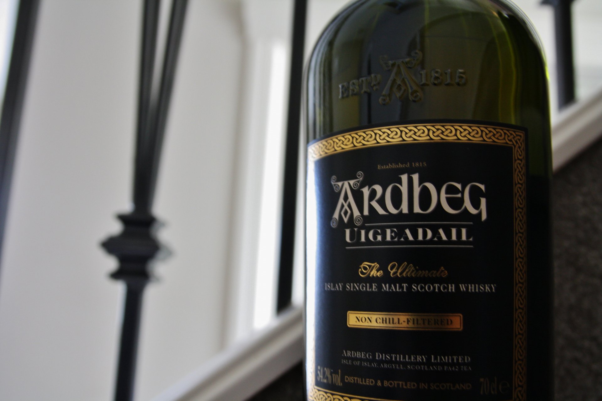 Close-up of an Ardbeg Uigeadail malt Scotch whisky bottle, showcased in sharp 4K Ultra HD detail against a blurred indoor background.