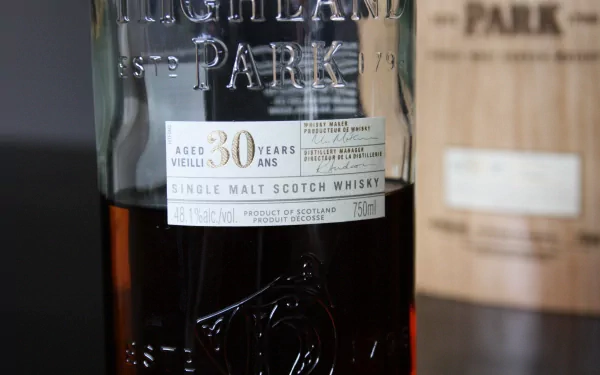 4K Ultra HD PC desktop wallpaper: close-up of a 30-year Highland Park single malt whisky bottle with a blurred wooden cask in the background — food & whisky theme.