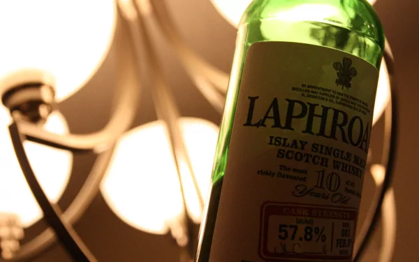 4K Ultra HD PC desktop wallpaper: close-up of a green Laphroaig whisky bottle tilted beside a warm chandelier light, shallow depth-of-field, food and whisky theme.