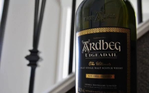 Close-up of an Ardbeg Uigeadail malt Scotch whisky bottle, showcased in sharp 4K Ultra HD detail against a blurred indoor background.