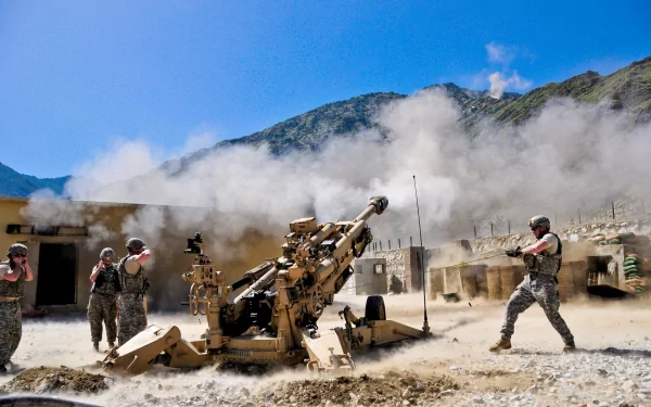 A soldier operates an M777 howitzer amid smoke and dust, showcasing military artillery in action against a mountainous backdrop. This HD wallpaper captures the intensity of war.