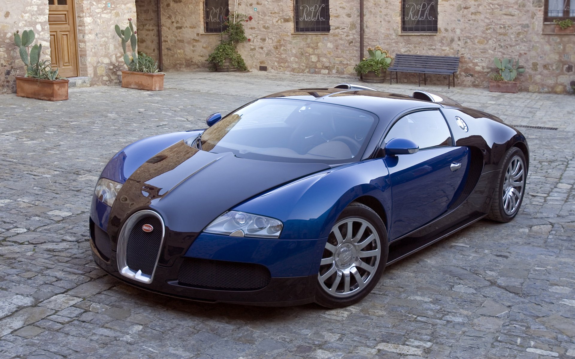 HD desktop wallpaper featuring a sleek blue and black Bugatti sports car parked on a cobblestone street.