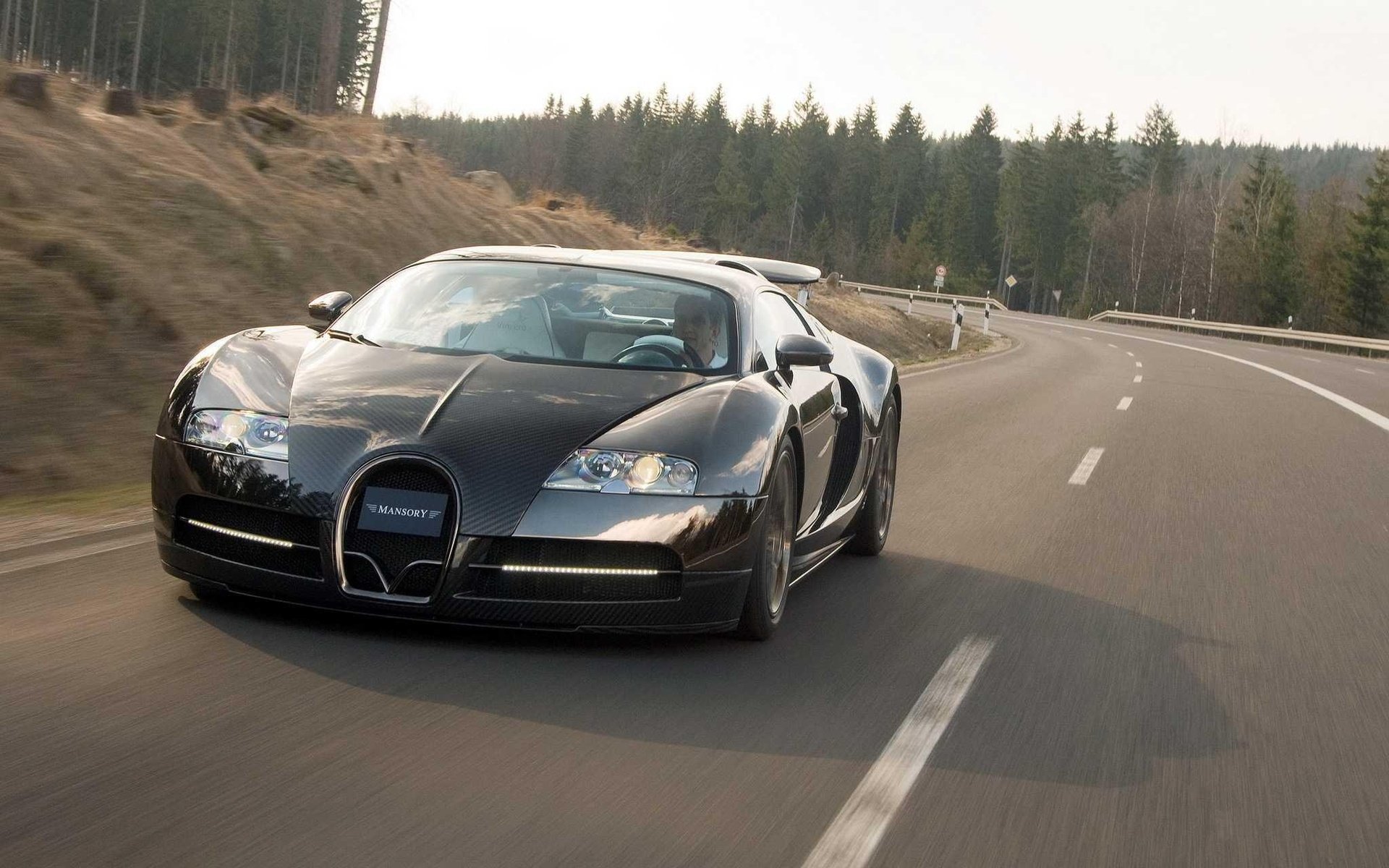 HD PC desktop wallpaper: black Bugatti Mansory car driving down a winding forest road.