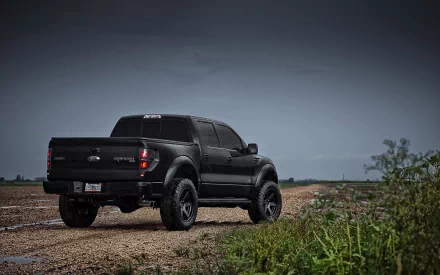 HD PC desktop wallpaper featuring a black Ford Raptor truck parked on a dirt road under a cloudy sky.
