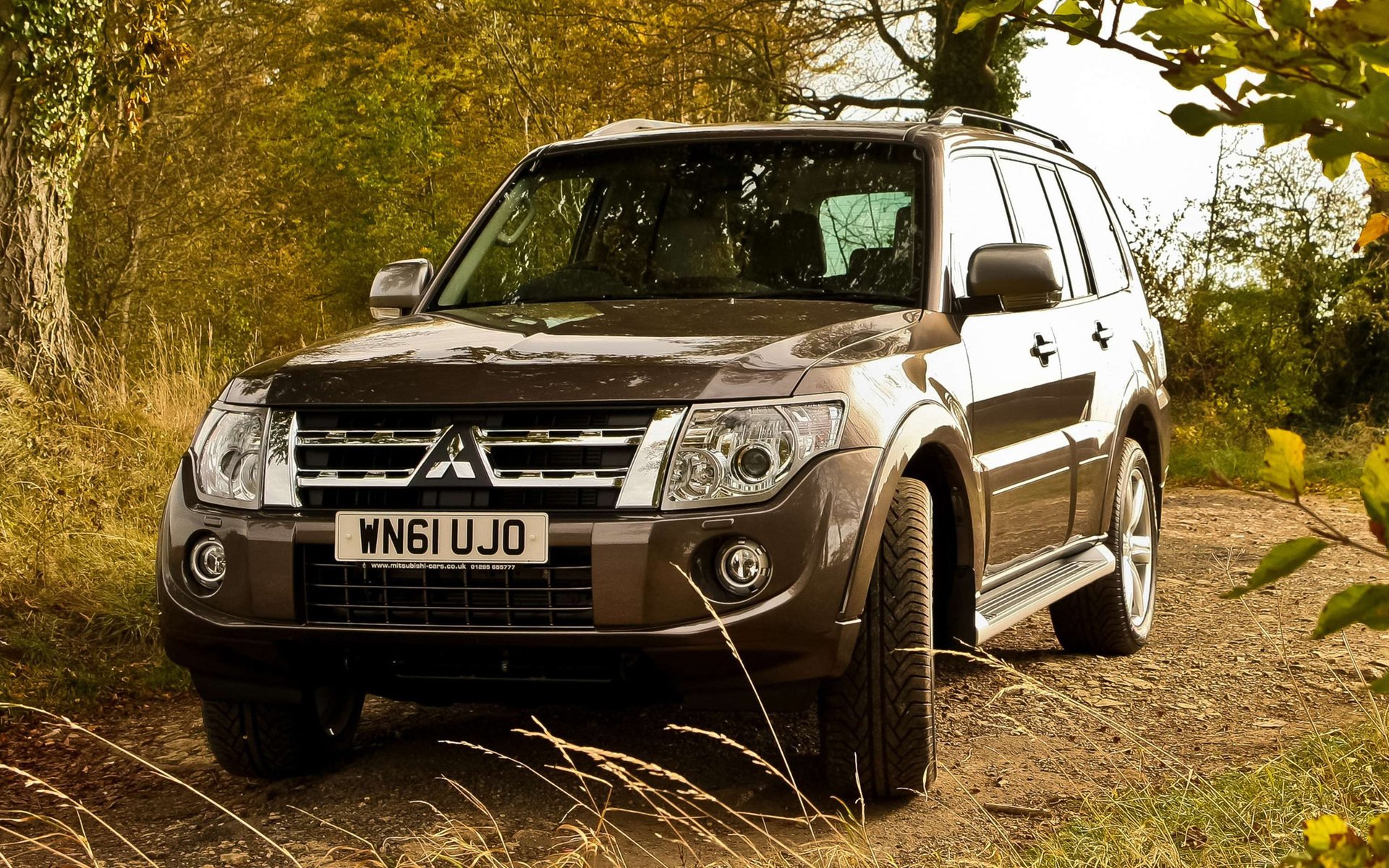 HD PC desktop wallpaper featuring a Mitsubishi SUV parked on a dirt path surrounded by autumn trees and foliage.