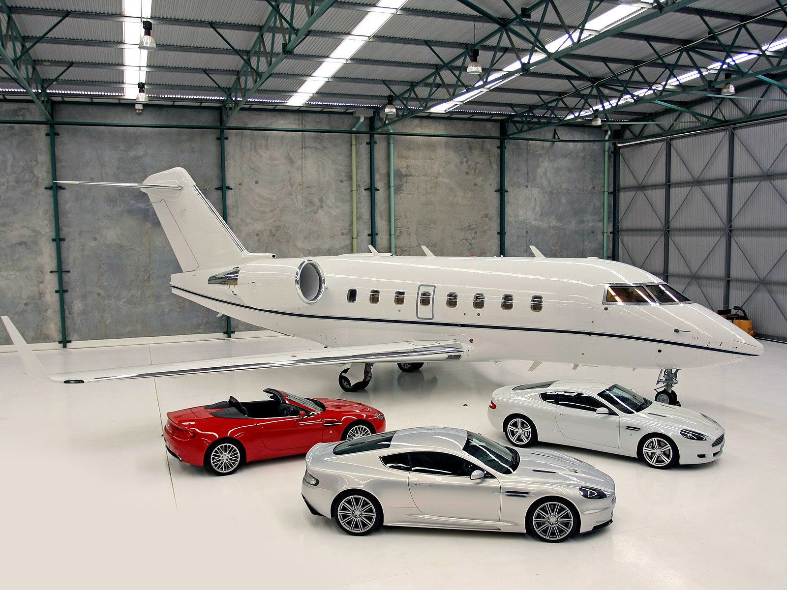 HD PC desktop wallpaper featuring a sleek Aston Martin vehicle collection displayed inside a spacious industrial hangar.