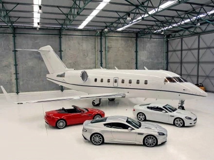 HD PC desktop wallpaper featuring a sleek Aston Martin vehicle collection displayed inside a spacious industrial hangar.