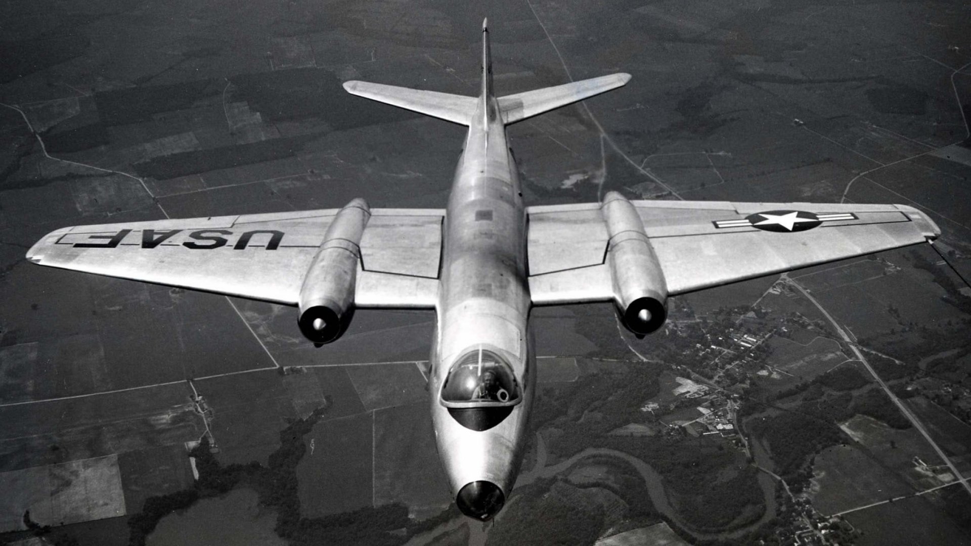HD desktop wallpaper showing a vintage military aircraft in flight with USAF markings over a rural landscape.