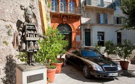 HD PC desktop wallpaper featuring a sleek Maybach vehicle parked beside a historic building with a detailed statue and potted plants in a sunlit courtyard.