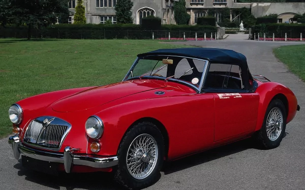 HD PC desktop wallpaper featuring a classic red MG convertible vehicle parked on a driveway with a large building and green lawn in the background.
