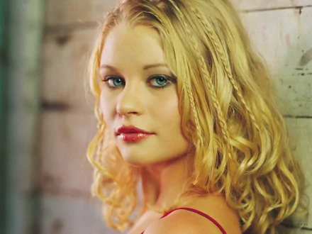 HD desktop wallpaper featuring celebrity Emilie De Ravin with blonde, curly hair, looking over her shoulder against a rustic wooden background.