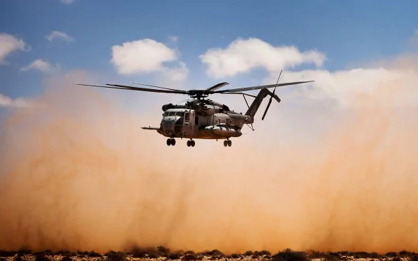 HD military desktop wallpaper featuring a Sikorsky CH-53E Super Stallion helicopter hovering above dusty terrain under a blue sky with scattered clouds.