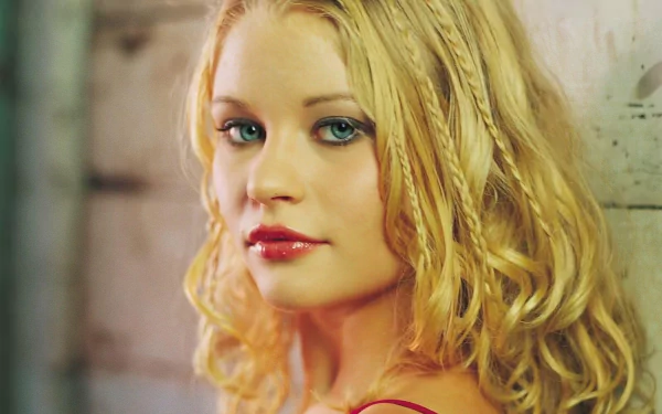 HD desktop wallpaper featuring celebrity Emilie De Ravin with blonde, curly hair, looking over her shoulder against a rustic wooden background.