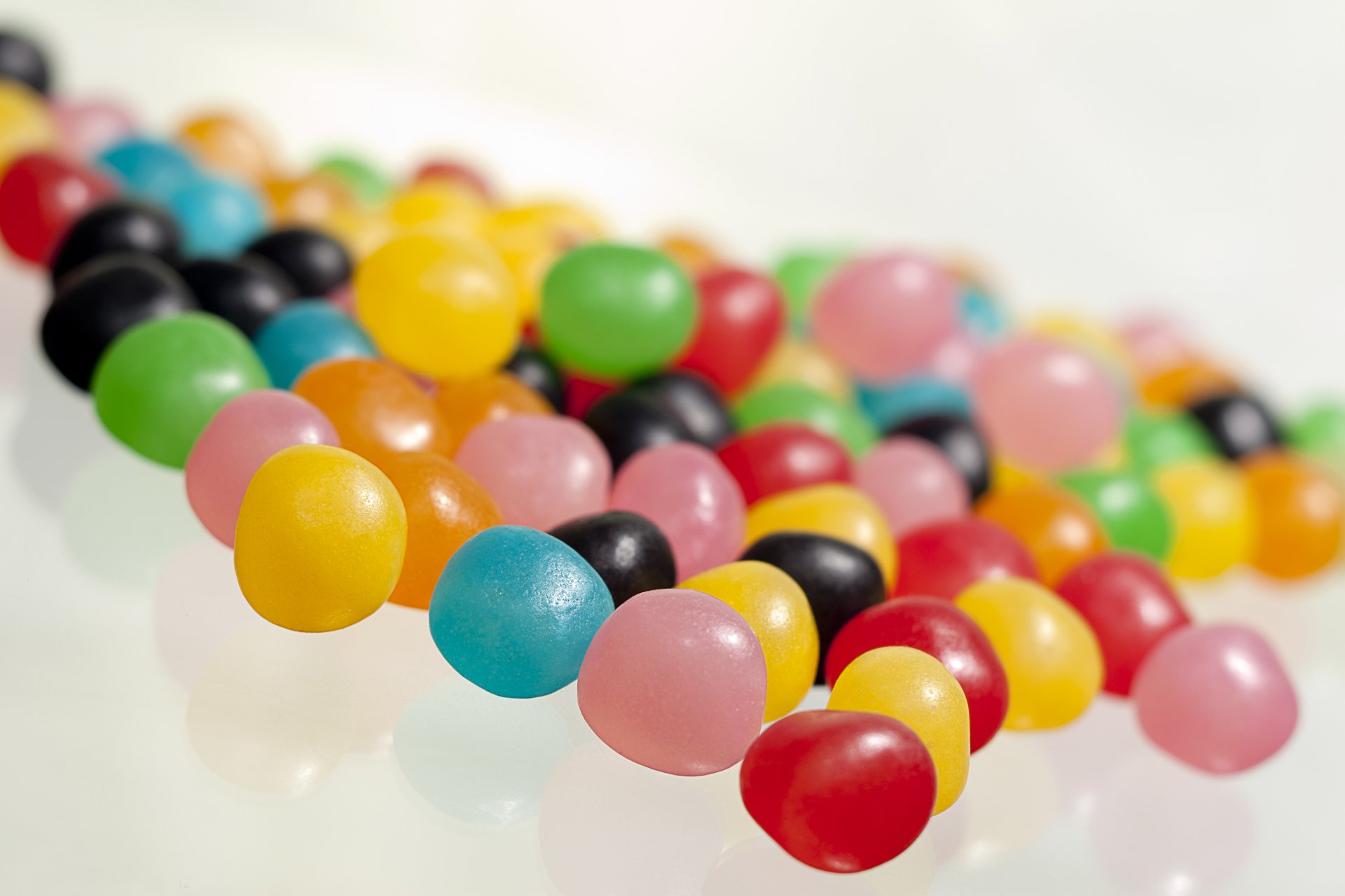 HD PC desktop wallpaper featuring colorful round candies in vibrant shades of yellow, green, pink, red, blue, and black scattered on a white surface.