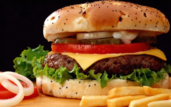 A close-up of a delicious burger featuring lettuce, tomato, pickles, and cheese, served with fries, set against a dark background. This image serves as an enticing HD desktop wallpaper.
