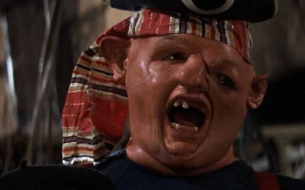 HD PC desktop wallpaper of The Goonies movie character Sloth — close-up of a pirate-hatted, scarred face with a gap-tooth grin against a dim ship interior background.