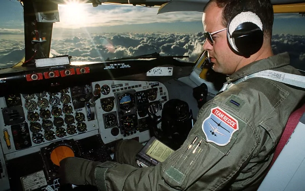 Pilot operating the cockpit of a Boeing KC-135 Stratotanker military aircraft, with sunlight filtering through clouds outside, shown in an HD desktop wallpaper.