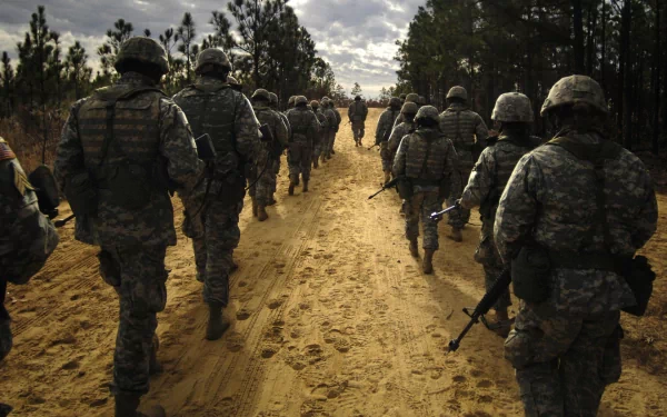 HD PC desktop wallpaper: military soldiers in full combat gear marching along a sandy forest road toward a distant horizon under a cloudy sky.