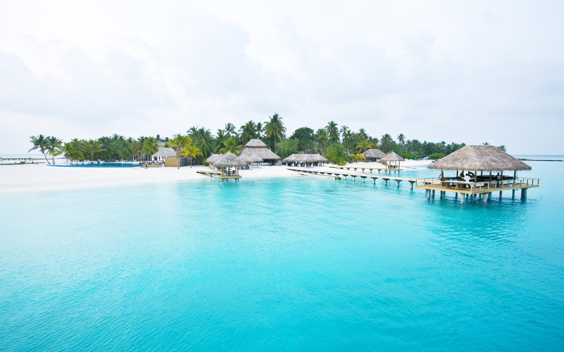 HD PC desktop wallpaper of a tropical Maldives scene: overwater huts, palm trees and clear turquoise ocean water in a serene photography background.