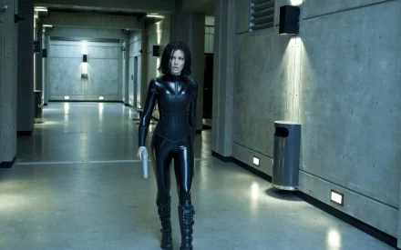 HD PC desktop wallpaper from the movie Underworld: Awakening, featuring a woman in a black leather outfit walking through a dimly lit industrial hallway.