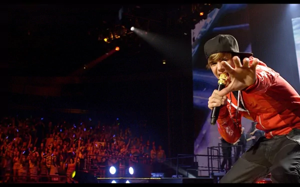 HD desktop wallpaper of Justin Bieber performing on stage, dressed in a red shirt and black cap, with an enthusiastic crowd and vibrant stage lights in the background. Tags: music, Justin Bieber.