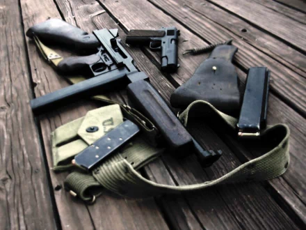 HD desktop wallpaper featuring a vintage submachine gun and handgun, laid out on a wooden surface with a holster, magazine, and belt. Man-made firearms displayed in high definition for background use.