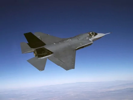 A high-definition desktop wallpaper featuring a Lockheed Martin F-35 Lightning II jet soaring through a clear blue sky.