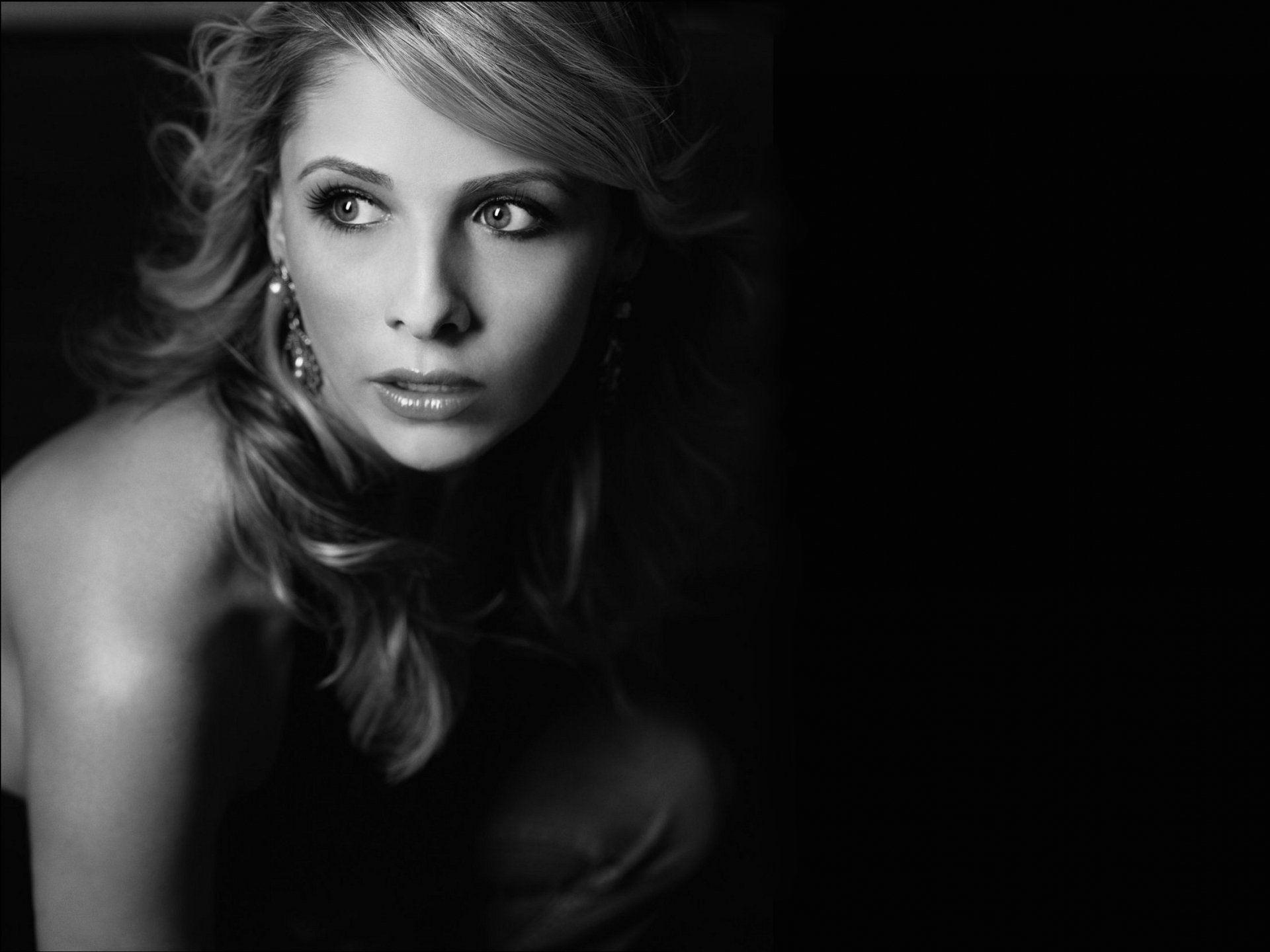 Black and white HD desktop wallpaper featuring celebrity Sarah Michelle Gellar, gazing thoughtfully to the side, with soft waves in her hair and intricate earrings. The background is dark, highlighting her profile.