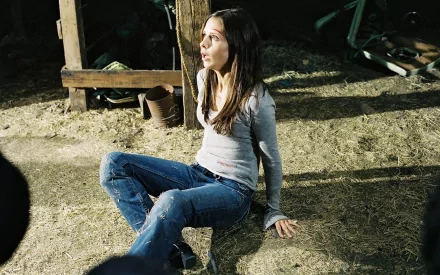 Sarah Michelle Gellar in a scene from the movie The Return (2006), seated on the ground in a dimly lit space with a look of concern on her face, creating a haunting atmosphere.