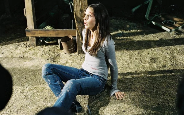 Sarah Michelle Gellar in a scene from the movie The Return (2006), seated on the ground in a dimly lit space with a look of concern on her face, creating a haunting atmosphere.