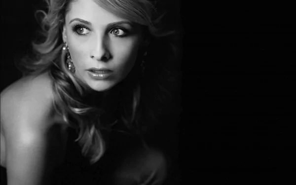 Black and white HD desktop wallpaper featuring celebrity Sarah Michelle Gellar, gazing thoughtfully to the side, with soft waves in her hair and intricate earrings. The background is dark, highlighting her profile.