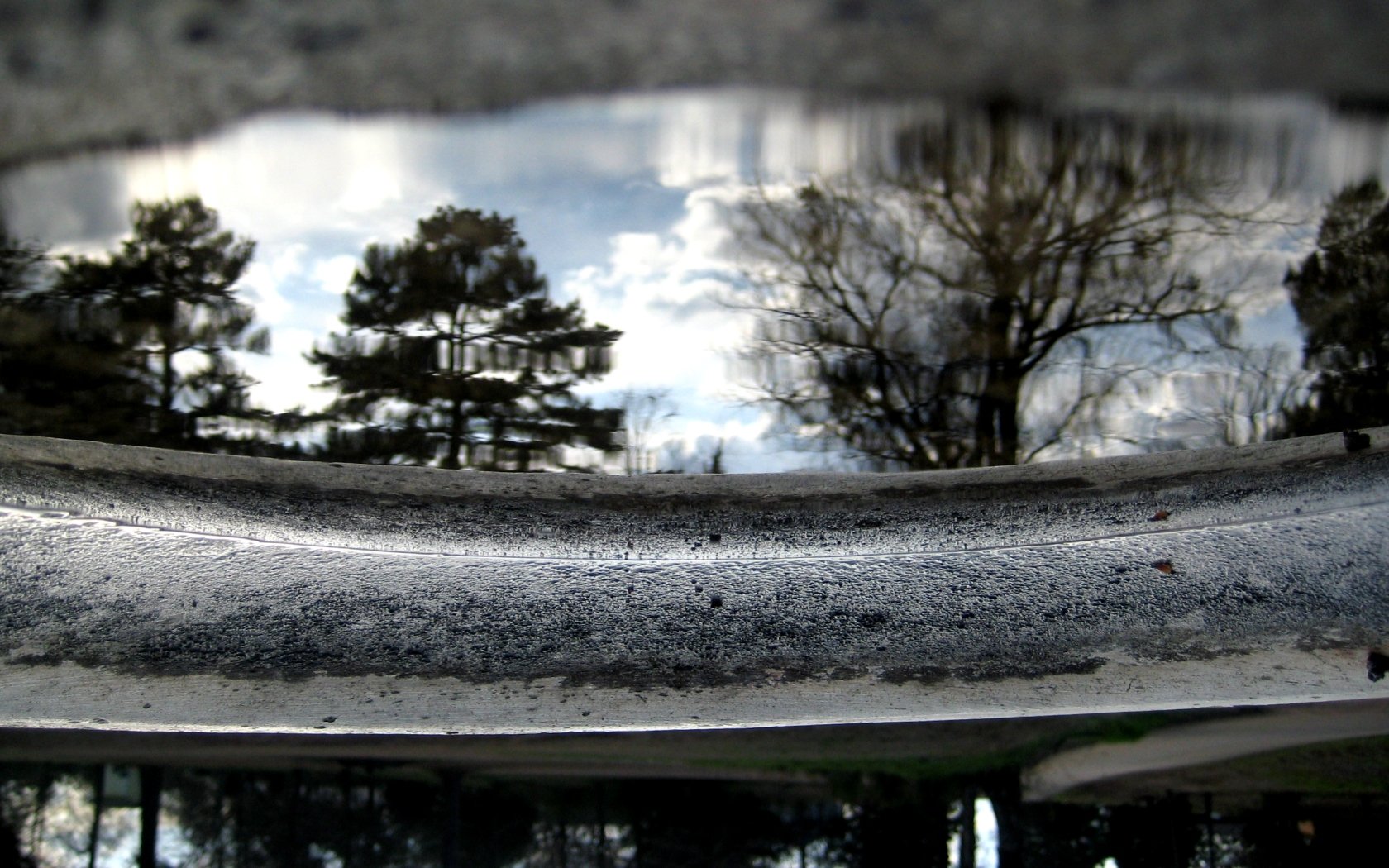 A close-up of a reflective surface showcasing trees and clouds mirrored on water, capturing the beauty of nature in an HD desktop wallpaper format.