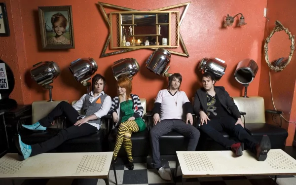 HD PC wallpaper featuring the band Paramore seated in a vintage salon setting, surrounded by retro hairdryers and a warm orange backdrop.