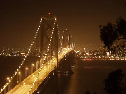 Night view of the illuminated Bay Bridge in San Francisco, showcasing man-made architecture with city lights glowing in the background, captured in HD quality.