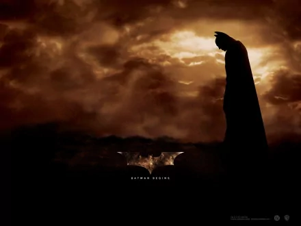 HD desktop wallpaper of a Batman Begins scene, featuring Batman silhouetted against a dramatic, cloudy sky. The background highlights the iconic Batman symbol and the movie title at the bottom.