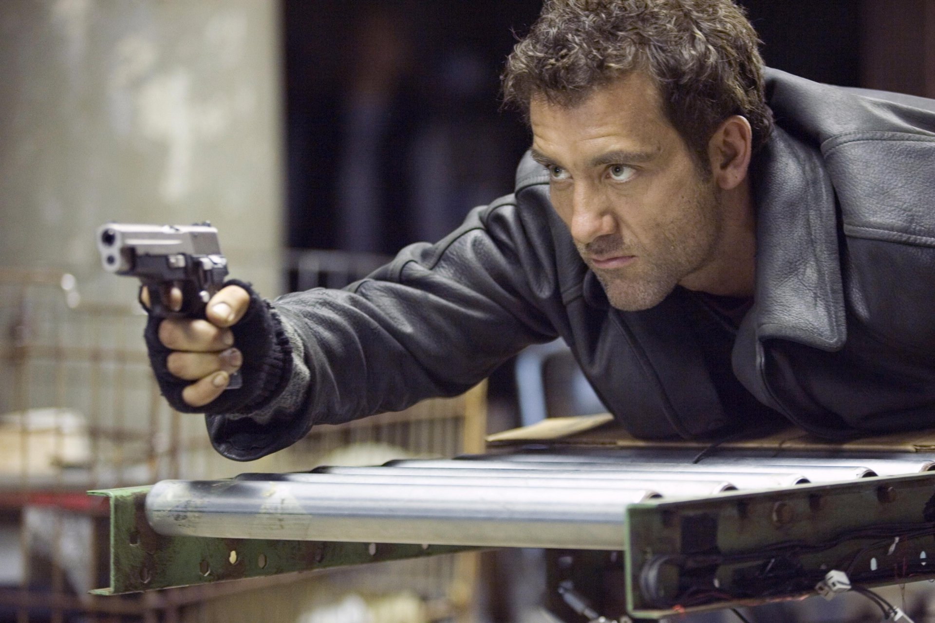 Clive Owen aiming a gun in a scene from the movie Shoot 'em Up, featured as a HD PC desktop wallpaper and background.