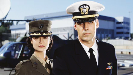 HD PC desktop wallpaper featuring two characters from the TV show JAG dressed in military uniforms with a helicopter and hangar in the background.