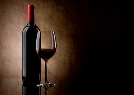 A sleek bottle of red wine stands beside a filled wine glass, set against a warm, muted background, creating an elegant ambiance in this 4K Ultra HD wallpaper.