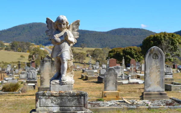 HD desktop wallpaper featuring a serene cemetery with a detailed angel statue standing among gravestones under a clear blue sky and distant hills.
