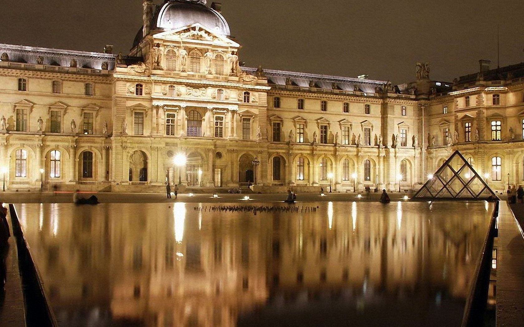 Night view of the illuminated Louvre Museum and its glass pyramid in Paris, reflected in the water, captured as an HD desktop wallpaper and background.